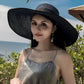 alt="Woman sitting on beach wearing black hat">