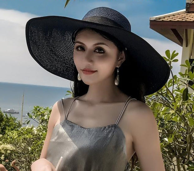 alt="Woman sitting on beach wearing black hat">